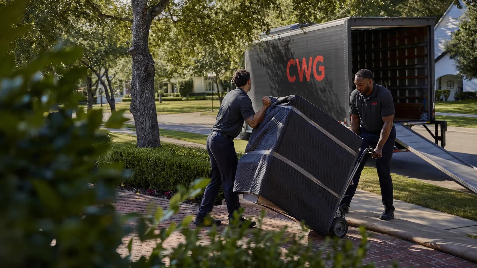 CWG two-person delivery team moving a blanket-wrapped appliance up the walk of a Houston home